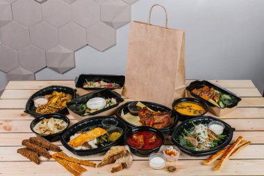 Paket servis kutularında çeşitli hazır yemekler ve ahşap bir masada hazır yemek seçenekleri sunan bir kese kağıdı.