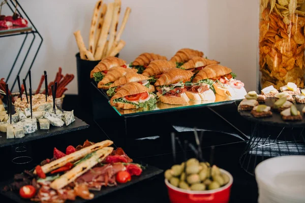 Yemek büfesi masasında çeşitli aperatifler, kruvasan sandviçler, peynir ve misafirler için şarküteri de dahil olmak üzere taze yiyecekler sunuluyor.