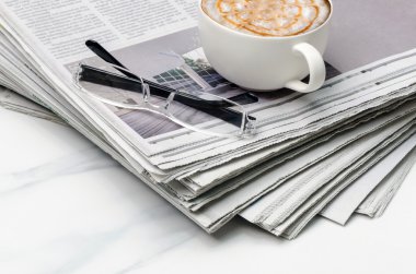 Gazete, fincan kahve ve gözlük masanın üzerine yığını.