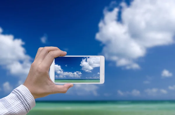 Mano de hombre con teléfono inteligente tomar fotos el cielo azul y el mar . —  Fotos de Stock