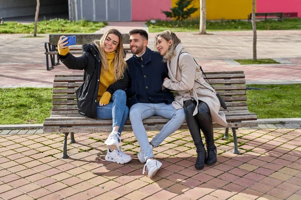Parktaki bankta oturan gülümseyen üç genç arkadaş. İki kız ve bir oğlan akıllı telefonlarıyla kendi portrelerini çekiyorlar. Sokakta poz veren mankenler. Arkadaşlık ve teknoloji kavramı