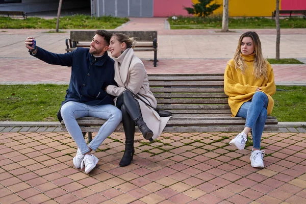 Kızgın bir kız onlara bakarken çift cep telefonlarıyla kendi portresini çekiyor. Kıskanıyor.