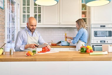 Genç ve mutlu bir çift sağlıklı bir yemek hazırlıyor. Adam sebze doğruyor, kadın spagetti pişiriyor.. 