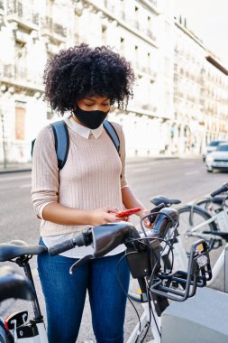 Bisiklet kiralamak için akıllı telefonunu kullanan Afro-Amerikalı bir kadın. Çevre dostu ulaşım kavramı
