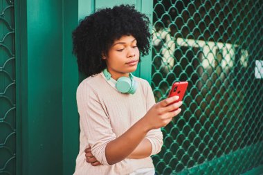 Yeşil duvarda akıllı telefon kullanan Afro saçlı bir kadın. Yaşam tarzı kavramı