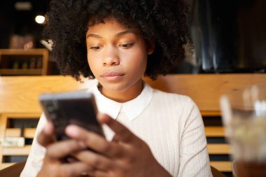 Kafede cep telefonu kullanan Afro-Amerikalı bir kadın. Latin bir kadın mesaj yazıyor.. 