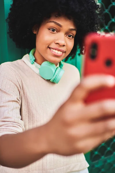 Afro haired woman with headphones using smart phone. Latin woman taking a self portrait. Lifestyle concept