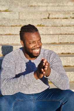 Güneşli bir günde merdivenlerde oturmuş gülümseyen Afrikalı Amerikalı bir adam. Mutlu genç Latin adam. Mutluluk kavramı
