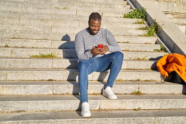 Pemuda Afrika Amerika duduk di tangga Mengirim pesan pada hari yang cerah. Orang kulit hitam melihat jaringan sosial pada ponsel pintar. — Stok Foto