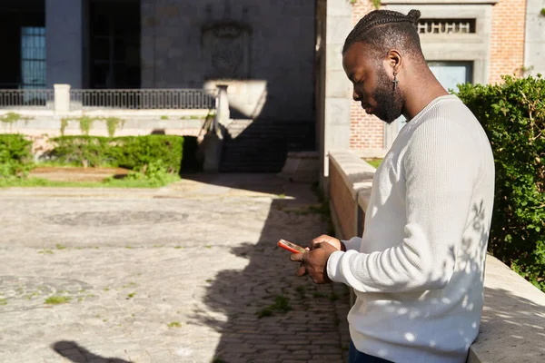 Handsome african american guy chatting via smartphone standing, cheerful dark-skinned man enjoined free time blogging in network via smartphone. — Stok Foto
