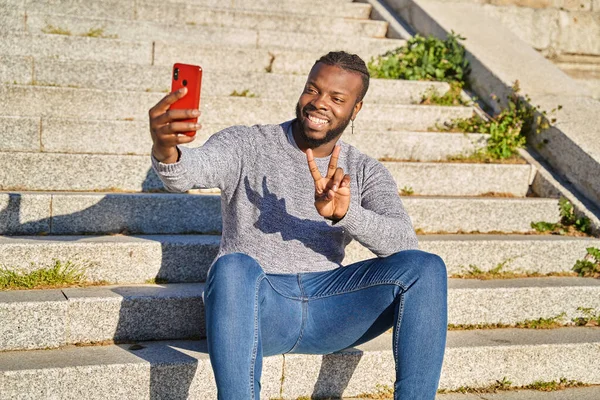 Jovem afro-americano sentado nas escadas tirando um auto-retrato com um smartphone. Homem negro feliz. Nova normalidade — Fotografia de Stock