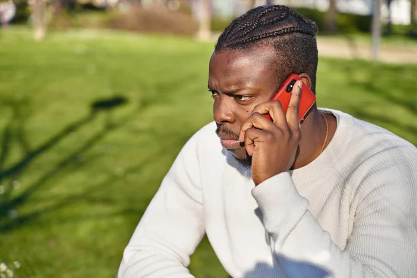 Retrato de um jovem afro-americano a falar ao telemóvel num parque. Homem negro com tranças no cabelo. — Fotografia de Stock