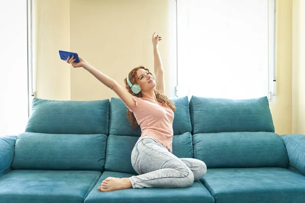 Glad ung kvinna som sitter på soffan med hörlurar. Kvinna eller tonåring flicka vilar, salighet njuta av att lyssna på musik på soffan hemma inredning i vardagsrummet. — Stockfoto