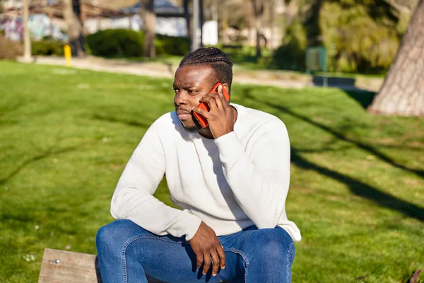 Pemuda Afrika-Amerika berbicara di ponsel di taman. Pria kulit hitam dengan kepang di rambutnya. — Stok Foto