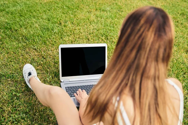 Visão traseira da jovem, sentada na grama, conversando com sua família usando um laptop, estudando, fazendo compras on-line, navegando na rede. Conceito de pessoas e tecnologia. — Fotografia de Stock