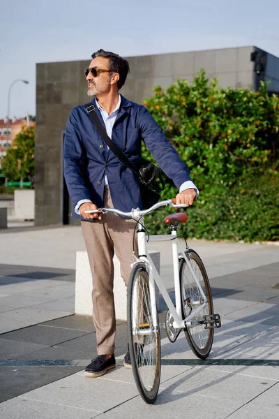 Vuxen man går till kontoret med ena handen håller cykeln och den andra handen tittar på sin mobiltelefon. Miljövänligt transportkoncept — Stockfoto