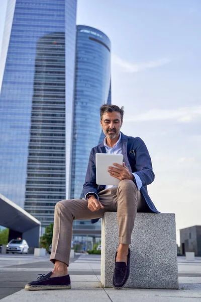 Uomo d'affari che legge e-mail ricevute su un tablet moderno mentre è seduto all'aperto di fronte a un edificio per uffici, uomo caucasico che controlla un messaggio su un pannello tattile digitale nel centro della città. — Foto Stock
