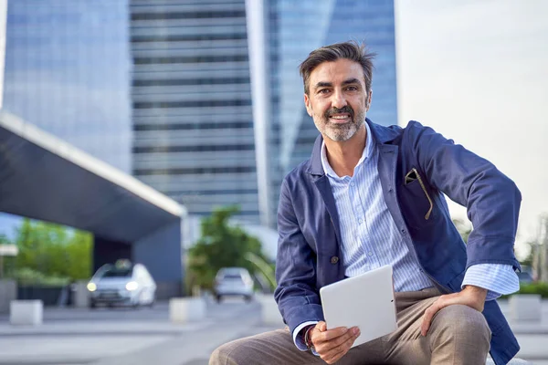 Empresário lendo e-mail recebido em um tablet moderno enquanto sentado ao ar livre em frente a um prédio de escritórios, homem caucasiano verificando uma mensagem em um painel de toque digital no centro da cidade. — Fotografia de Stock