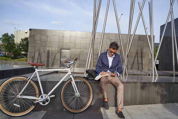 Pengusaha dewasa duduk di buku catatan menulis di buku catatan. Dia menggunakan sepeda untuk berkeliling kota ini. Konsep transportasi hijau. — Stok Foto