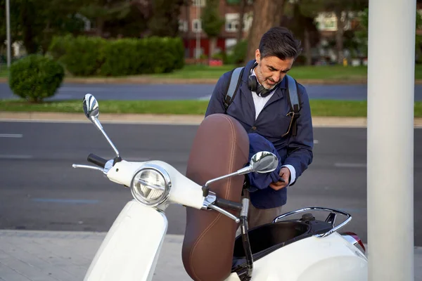 Pria dewasa mengambil helm keselamatan dari skuter putihnya. Konsep perlindungan pada sepeda motor. — Stok Foto