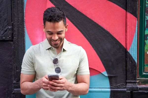 Jovem alegre latino cara mensagens, verificando redes sociais, conversando em seu telefone inteligente em fundo colorido. — Fotografia de Stock