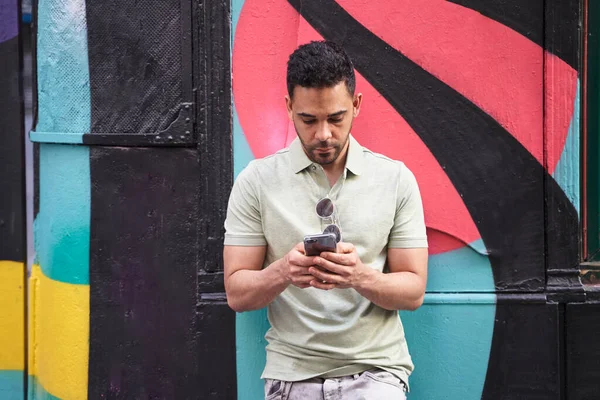 Genç Latin bir adam sosyal ağları kontrol ediyor, mesajlaşıyor, renkli arka planda akıllı telefonuyla sohbet ediyor.. 