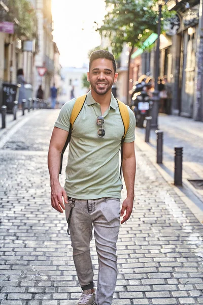 Jovem sorridente latino caminhando pelas ruas da cidade. Homem latino de jeans e camisa de pólo verde. — Fotografia de Stock