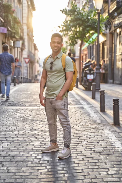 Muda tersenyum pria Latin berjalan melalui jalan-jalan kota. Pria Latin dengan celana jeans dan kemeja polo hijau. — Stok Foto