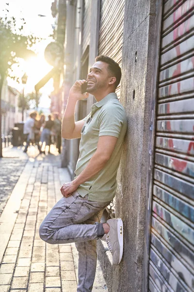 Homem latino encostado à parede a falar ao telemóvel. Retrato à luz de fundo. Conceito de comunicação. — Fotografia de Stock
