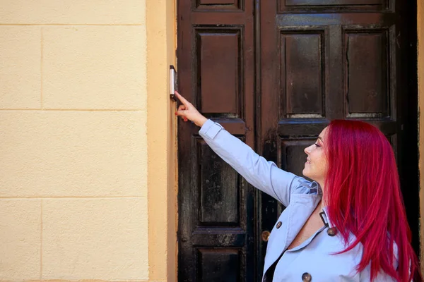 家のインターホンと呼ばれる青いトレンチコートの赤い髪の女性. — ストック写真
