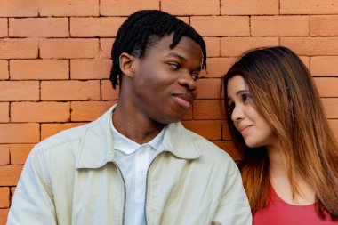 Genç, çok ırklı bir çift, tuğla bir duvarın yanında durup birbirlerine sevgi ve sevgiyle bakıyorlar.