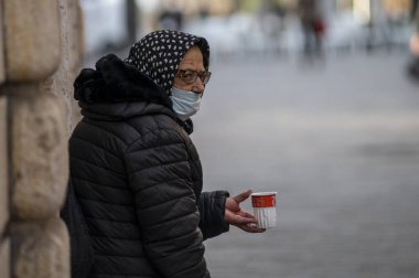 Şehir merkezinde tıbbi maskeli bir kadın dileniyor.