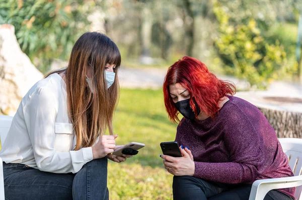 girls with medical mask using phone in the garden