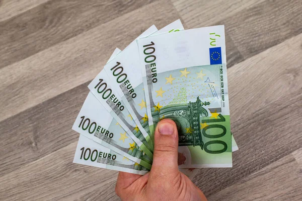 Człowiek Trzyma 100 Banknotów Euro Wentylatora Drewnianym Stole — Zdjęcie stockowe