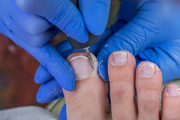 The nail technician processes the cuticle on the toe. Hardware pedicure in the salon.