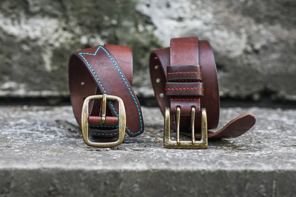 Two handmade brown leather belts with brass buckle. Genuine leather accessories for men. Horizontal photographs of objects.