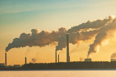 Gökyüzündeki fabrika bacalarından duman çıkıyor.