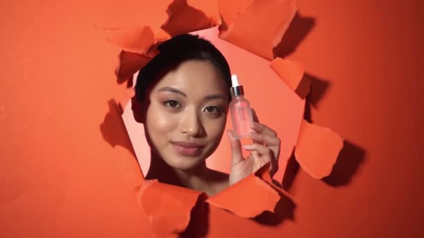 Счастливая Азиатка Держит Бутылку Сывороткой Рядом Разорванной Бумагой Оранжевый Фон — стоковое видео