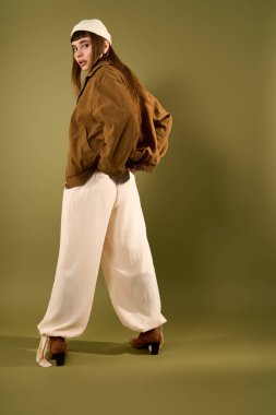 Şık, genç bir kadın, kendine güvenen, yeşil bir arka planı olan şık bir elbiseyle poz verir..