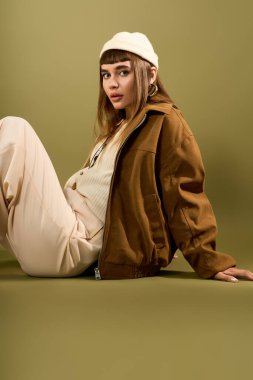 Güzel genç bir kadın zarif bir şekilde oturur şık bir ortamda şık kıyafetini sergiler..