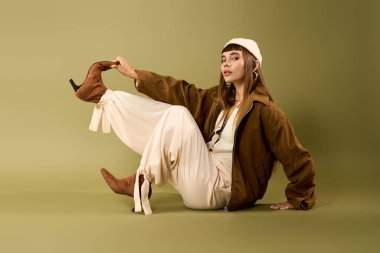 Genç, güzel bir kadın zarif bir şekilde yeşil bir zeminde otururken moda anlayışını sergiliyor..