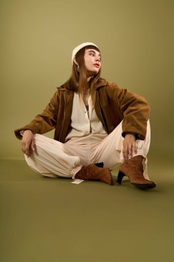 Şık görünümlü genç bir kadın zarif bir şekilde yeşil bir zeminde oturuyor ve kendine has tarzını sergiliyor..