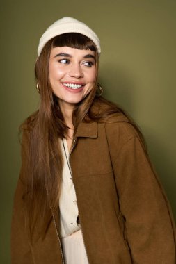 Genç bir kadın yeşil bir zemine karşı şık bir elbiseyle mutluluk saçar..