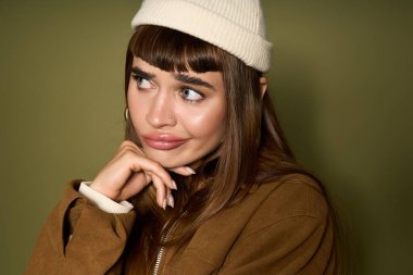 Neşeli görünüşlü genç ve güzel bir kadın, yeşil bir elbiseyle düşünceli bir şekilde poz verir..