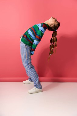 Kadın benzersiz bir poz sergiliyor, modaya uygun giyinerek mutluluk saçıyor ve canlı bir arka planı var..