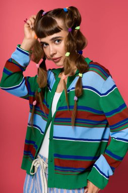 Atkuyruklu genç bir kadın şık çizgili bir hırkayla parlak bir arkaplanda poz veriyor..