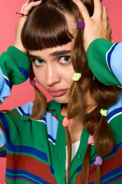 Genç bir kadın eşsiz saç örgüleri ve renkli bir kıyafetle canlı bir arkaplan karşısında tarzını sergiliyor..