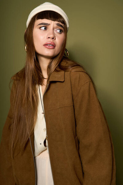 Красивая женщина с длинными волосами и модной одеждой задумчиво позирует перед зеленой стеной.