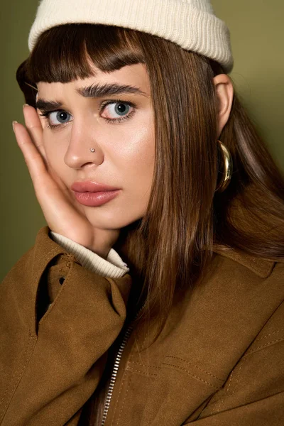 Göz alıcı özellikleri olan genç bir bayan şık bir kıyafet giymiş düşünceli bir şekilde poz veriyor..