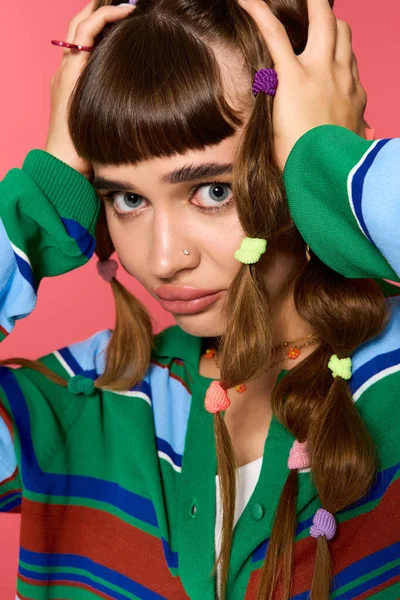 Genç bir kadın eşsiz saç örgüleri ve renkli bir kıyafetle canlı bir arkaplan karşısında tarzını sergiliyor..